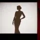 سایه‌ روشن یک سلبریتی زن با لباس مجلسی شیک روی پرده سفید سینما، در صحنه‌ای نمادین با پرده‌های مخمل قرمز کنار رفته از زاویه روبه‌رو
